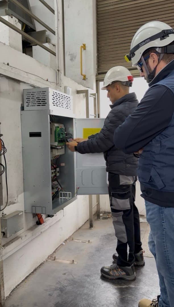 Dos técnicos revisando el tablero de control junto a la máquina de tracción